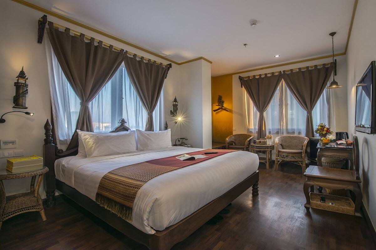 Una habitación de hotel con una cama grande, dos sillas, una mesita pequeña y una mesita de noche.