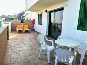 A small outdoor patio with two yellow lounge chairs, a white plastic chair, and a small round table. - Apartamentos Monteparaiso (Mogan)
