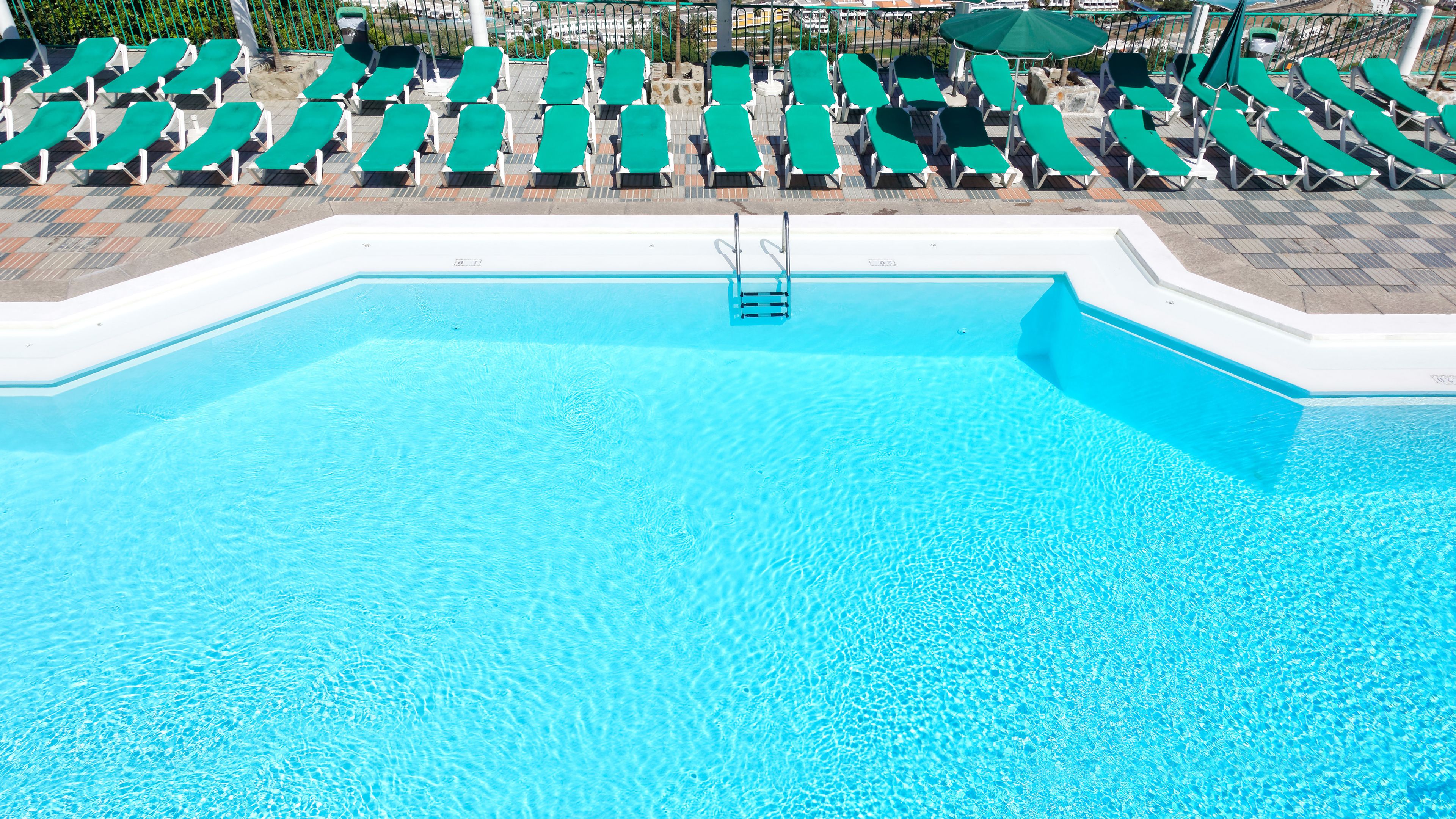 A swimming pool with clear blue water, surrounded by rows of green lounge chairs and umbrellas.