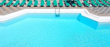 A swimming pool with clear blue water, surrounded by rows of green lounge chairs and umbrellas.