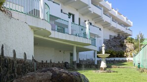 A multi-story building with balconies, a stone wall, and a fountain. - Apartamentos Monteparaiso (Mogan)