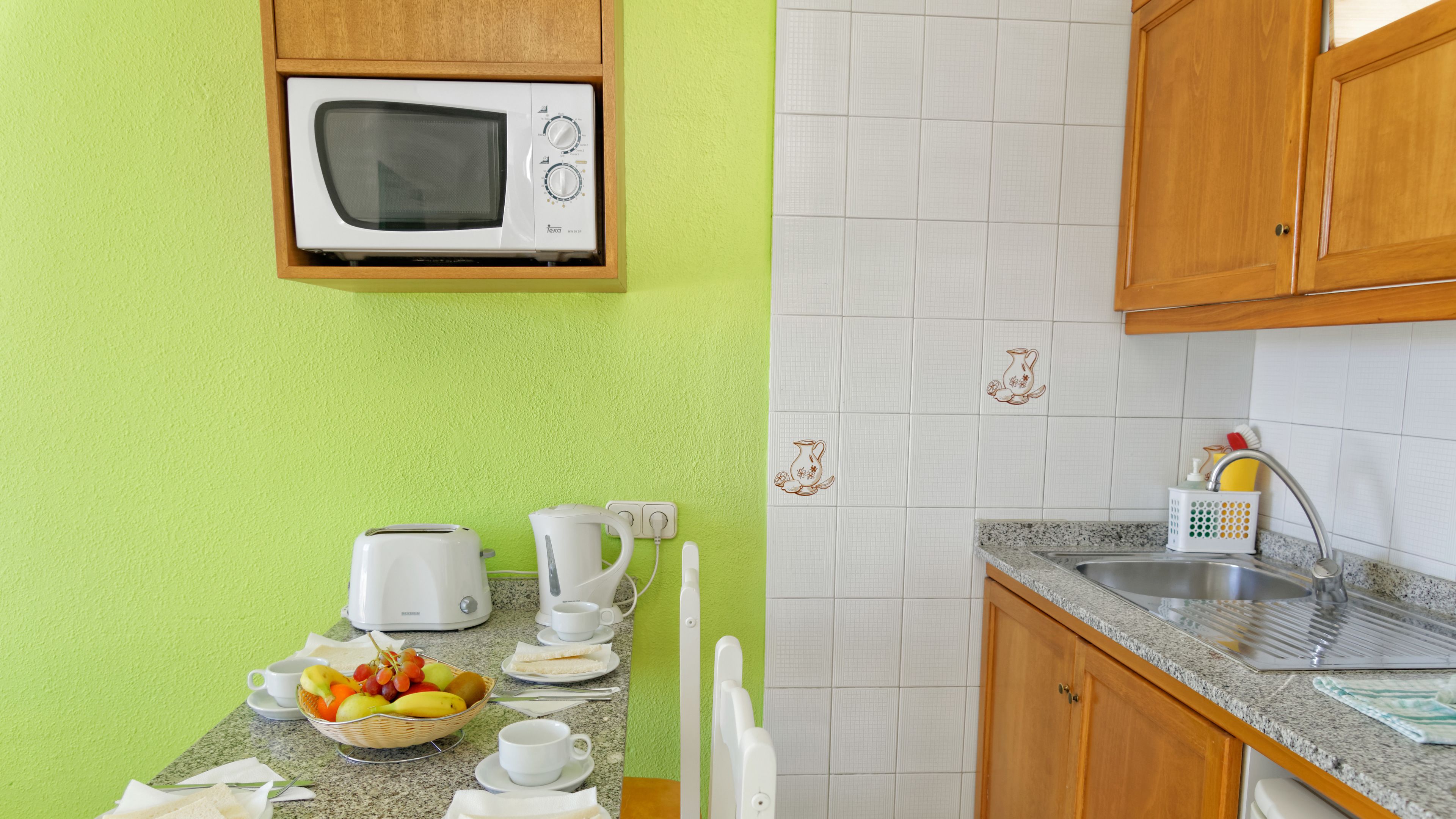 Cocina equipada con microondas, tostadora y pileta. Hay un frutero en la encimera y una taza de café.