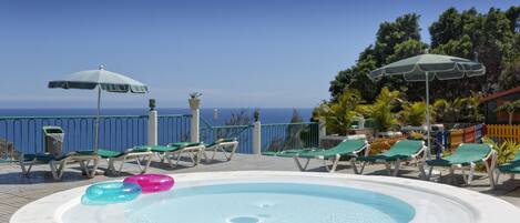 A pool area with lounge chairs and umbrellas, overlooking the sea.