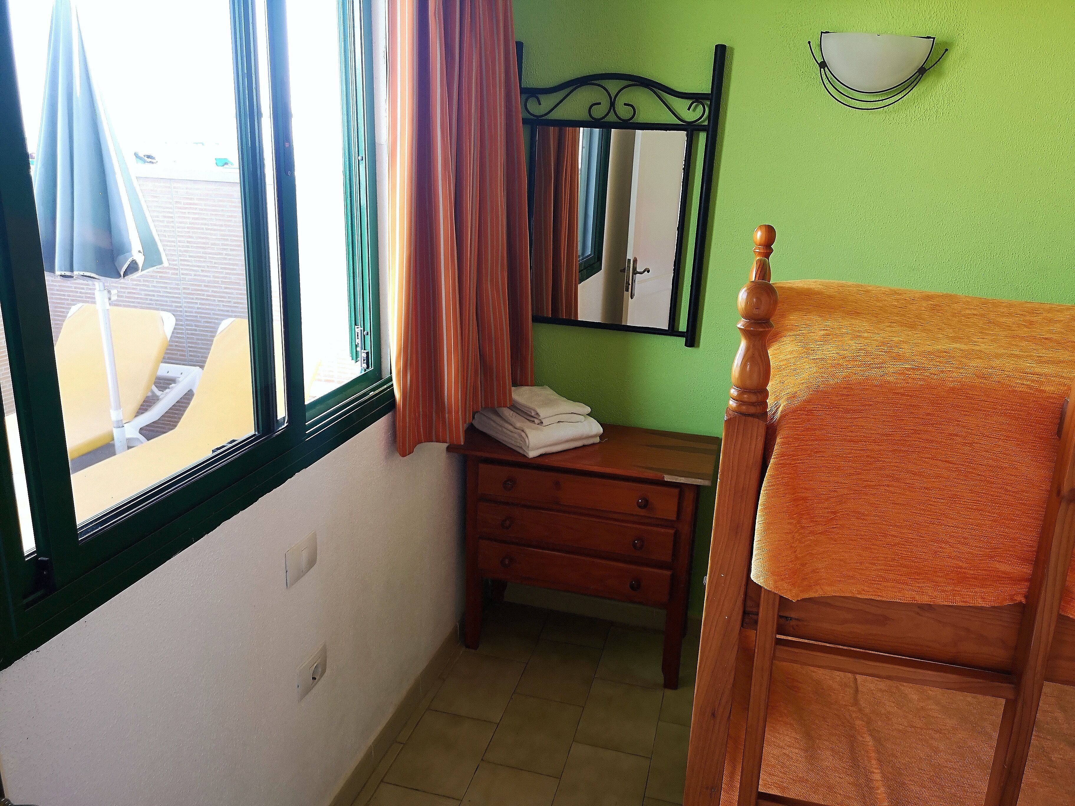Una habitación con cama, una mesita de noche de madera, un espejo y una ventana con cortinas.