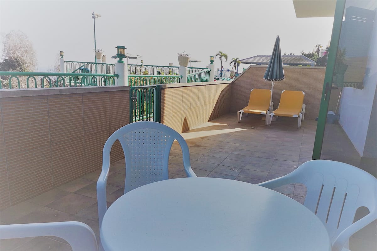 A terrace with a table and chairs, a green fence, and a brick wall.