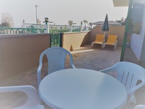 A terrace with a table and chairs, a green fence, and a brick wall. - Apartamentos Monteparaiso (Mogan)