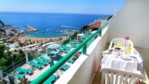 A balcony with a table set for breakfast overlooking a beach and marina. - Apartamentos Monteparaiso (Mogan)