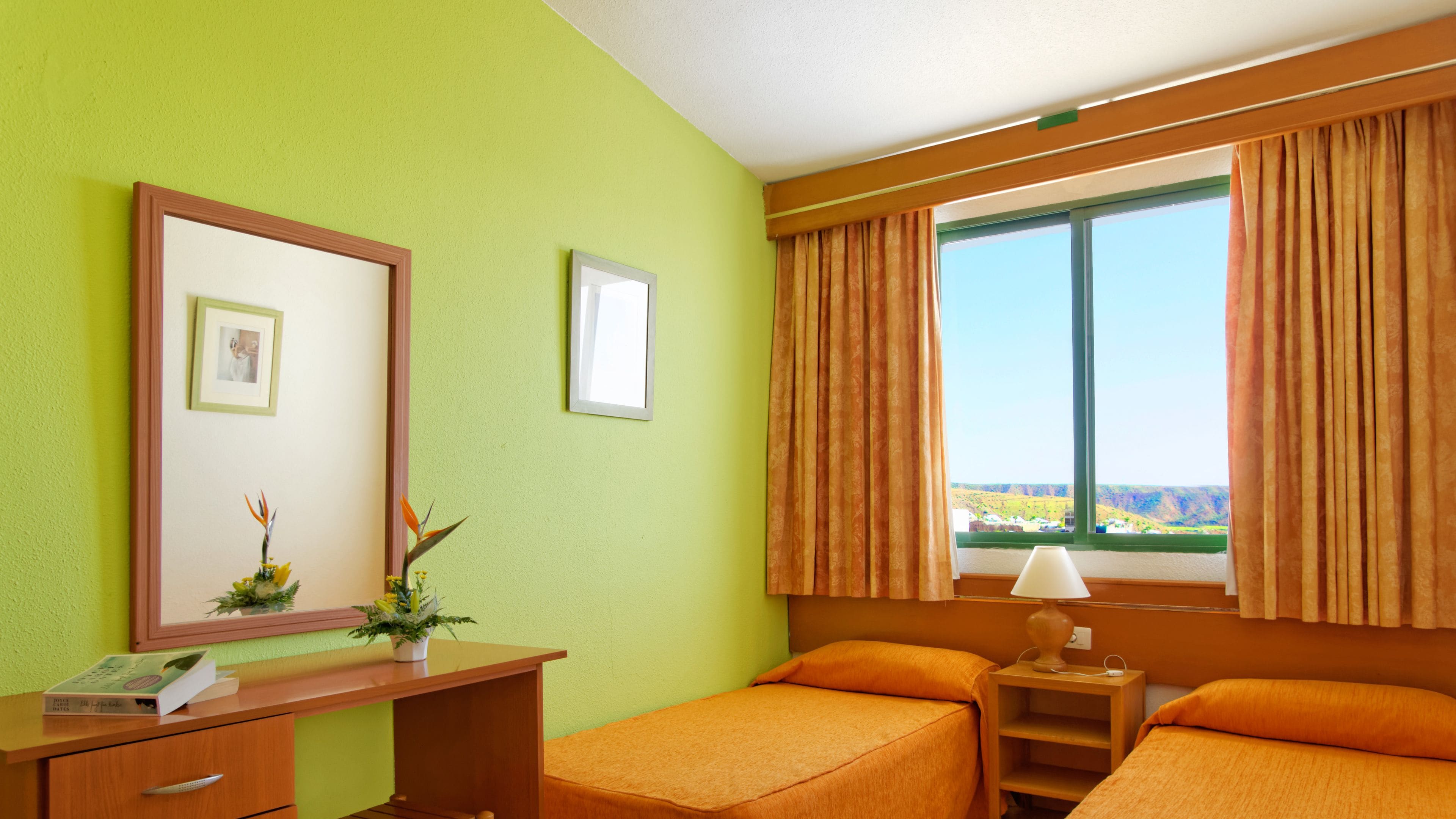 Una habitación de hotel con cama, escritorio, lámpara y ventana con cortinas.