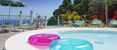 Zona de piscina con flotadores inflables, sillones de descanso y sombrillas.