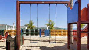 A playground with swings, sand, and a fenced area. - Apartamentos Monteparaiso (Mogan)