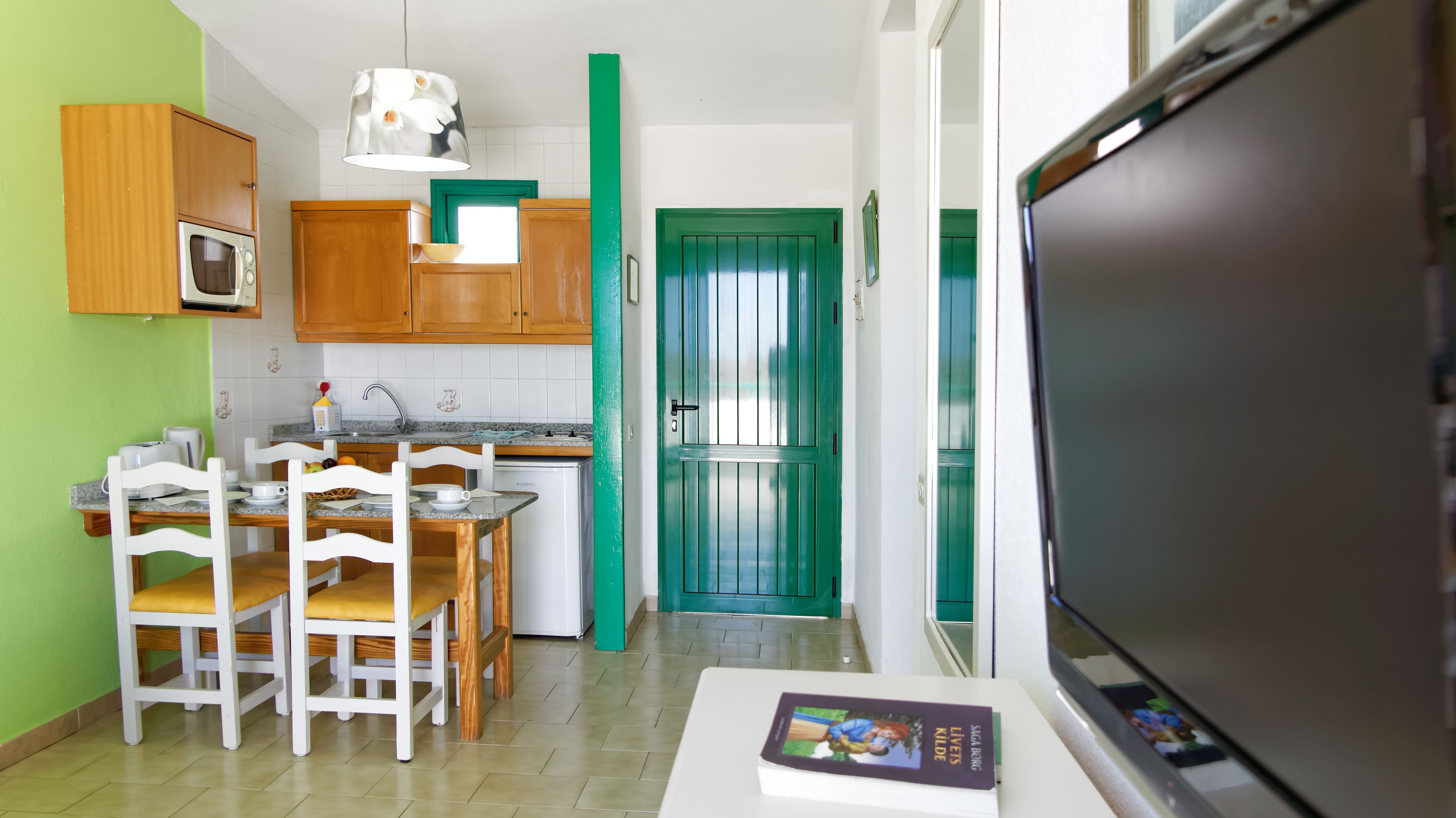 A compact kitchen with wooden cabinets, a microwave, a sink, and a dining area with chairs and a table.