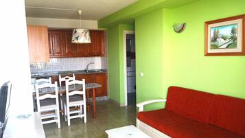 Una cocina con armarios de madera, una mesa de comedor con sillas, un sofá rojo y un cuadro en la pared.