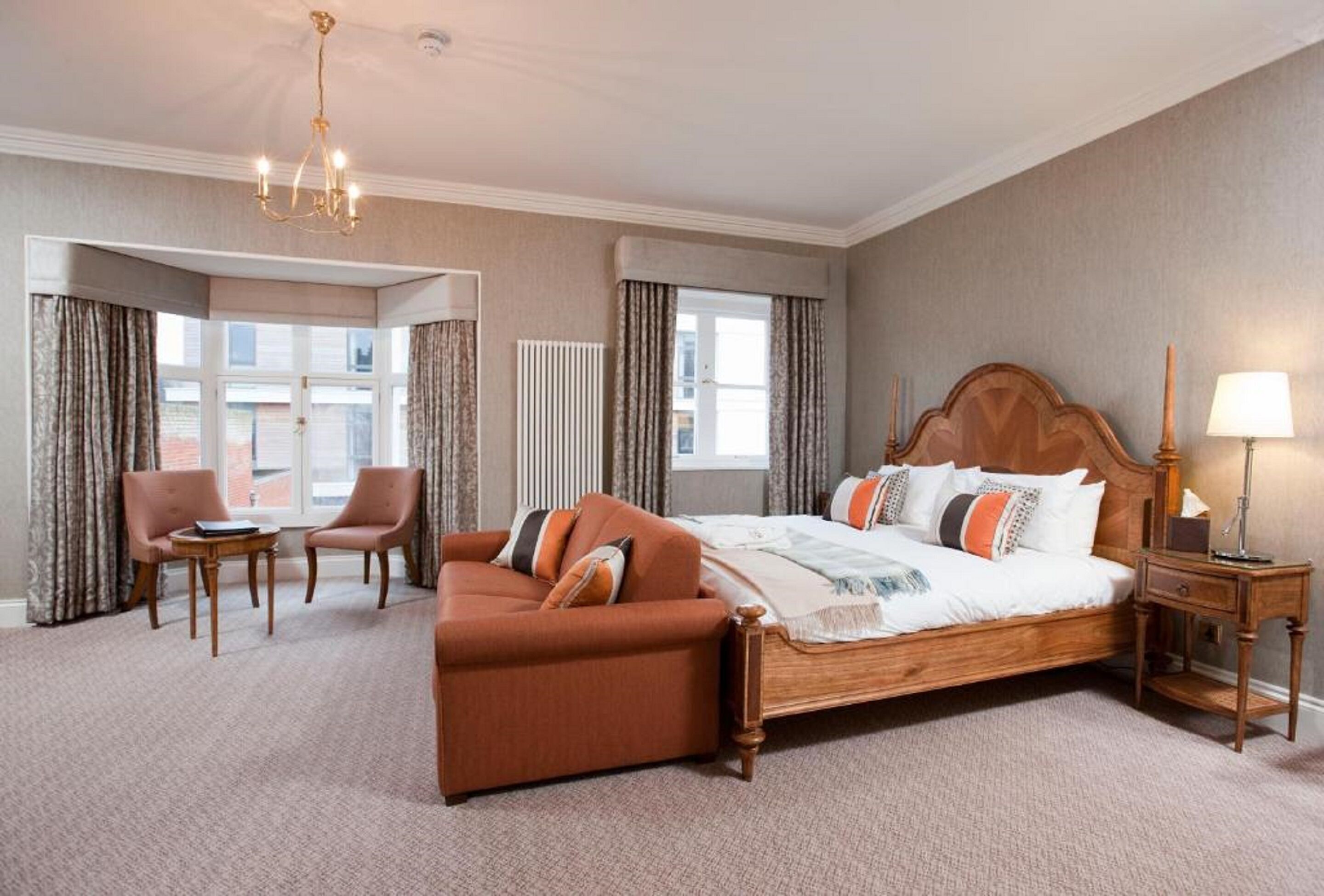 A hotel room with a large bed, a sofa, a small table, and a lamp.