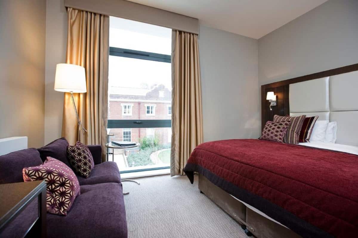 A hotel room with a bed, a sofa, a desk, and a window with curtains.