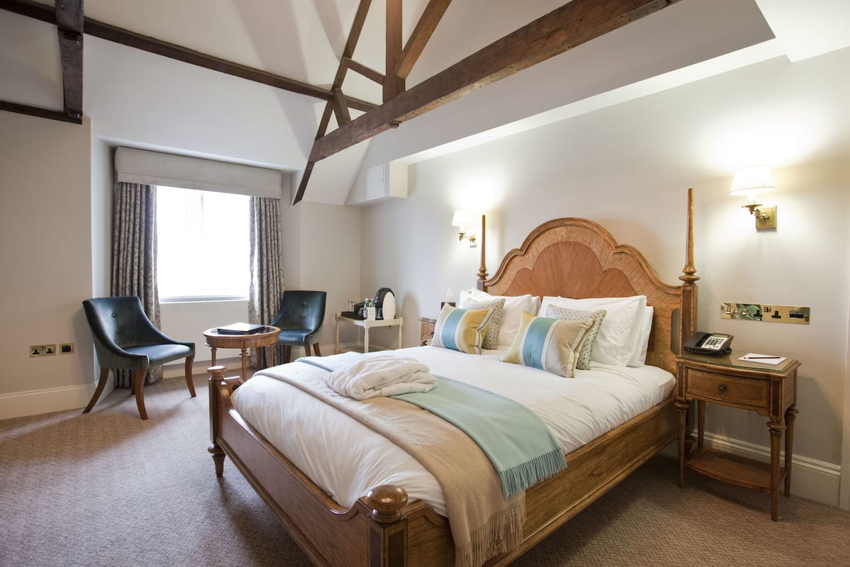 A bedroom with a wooden bed, a chair, a bedside table, and a lamp.