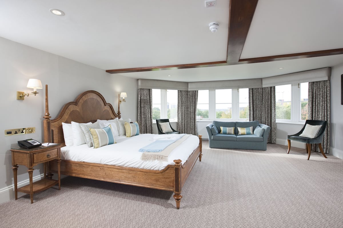 A spacious bedroom with a large bed, a sitting area with a sofa, and a view of the outdoors through large windows.