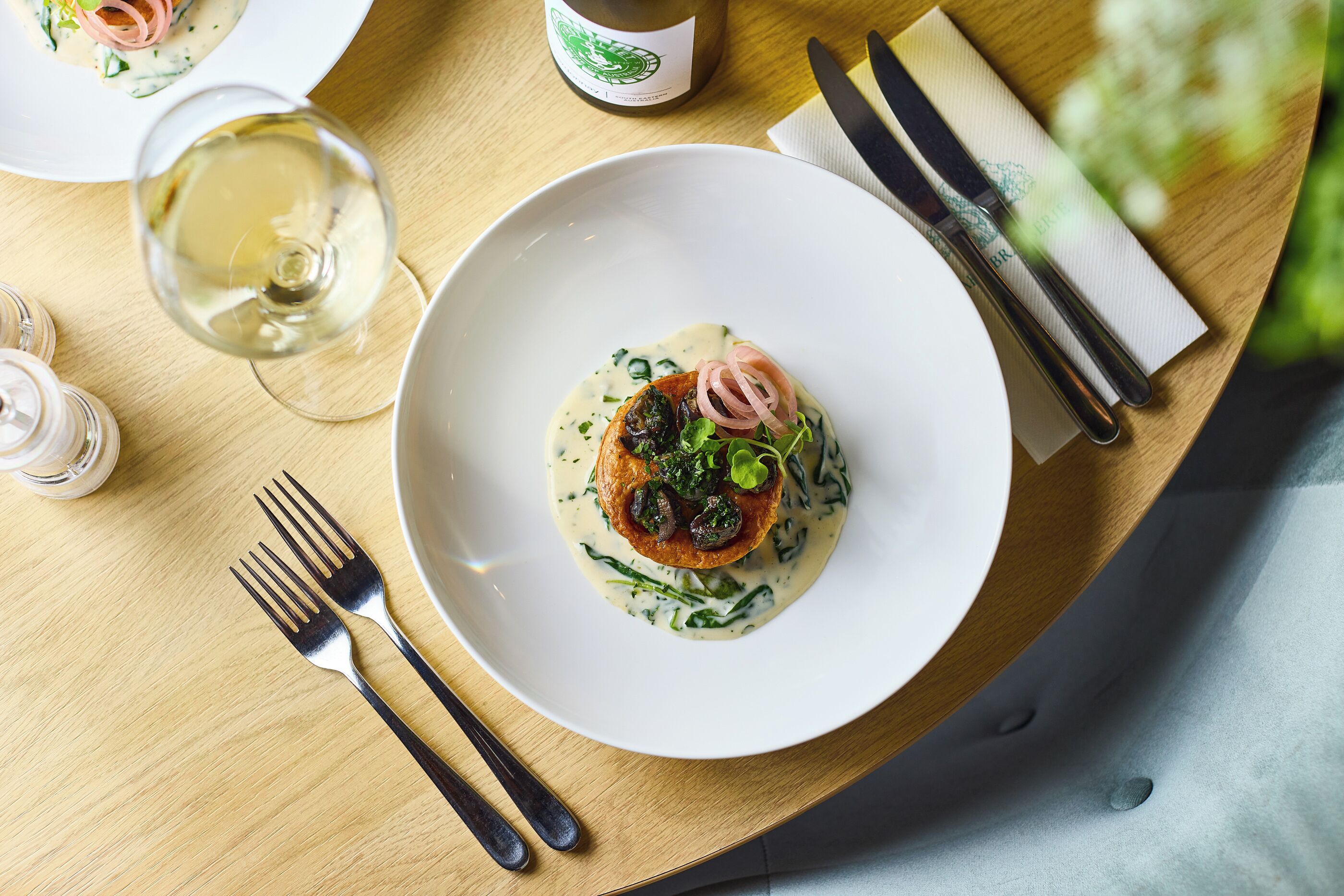 Una mesa de comedor con un plato de comida blanca, una copa de vino blanco y cubiertos.