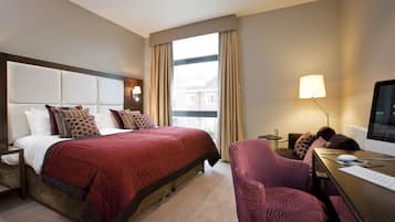 Habitación de hotel con una cama grande, un escritorio con computadora, una silla y una ventana con cortinas.