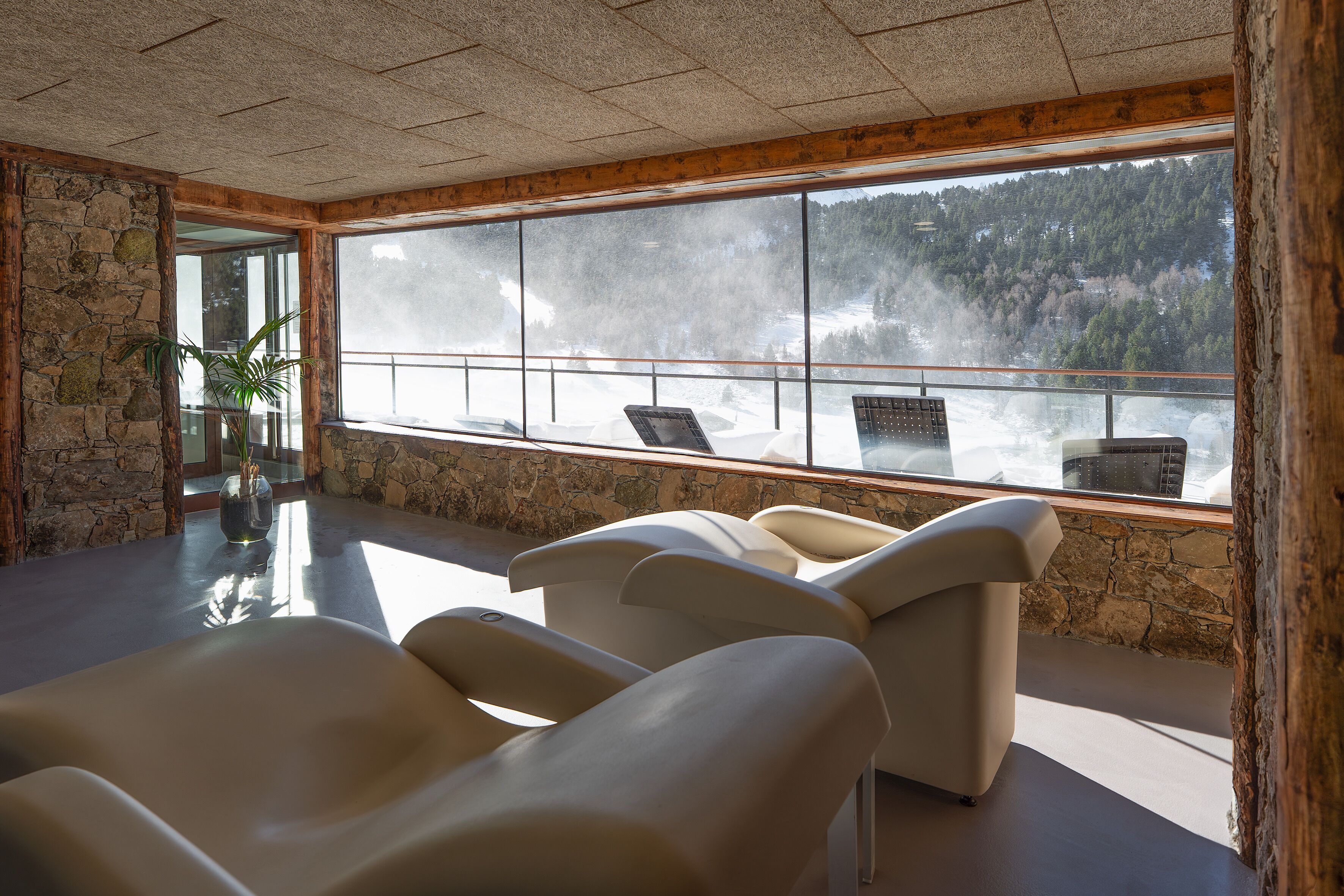 A room with stone walls, large windows, and modern chairs.