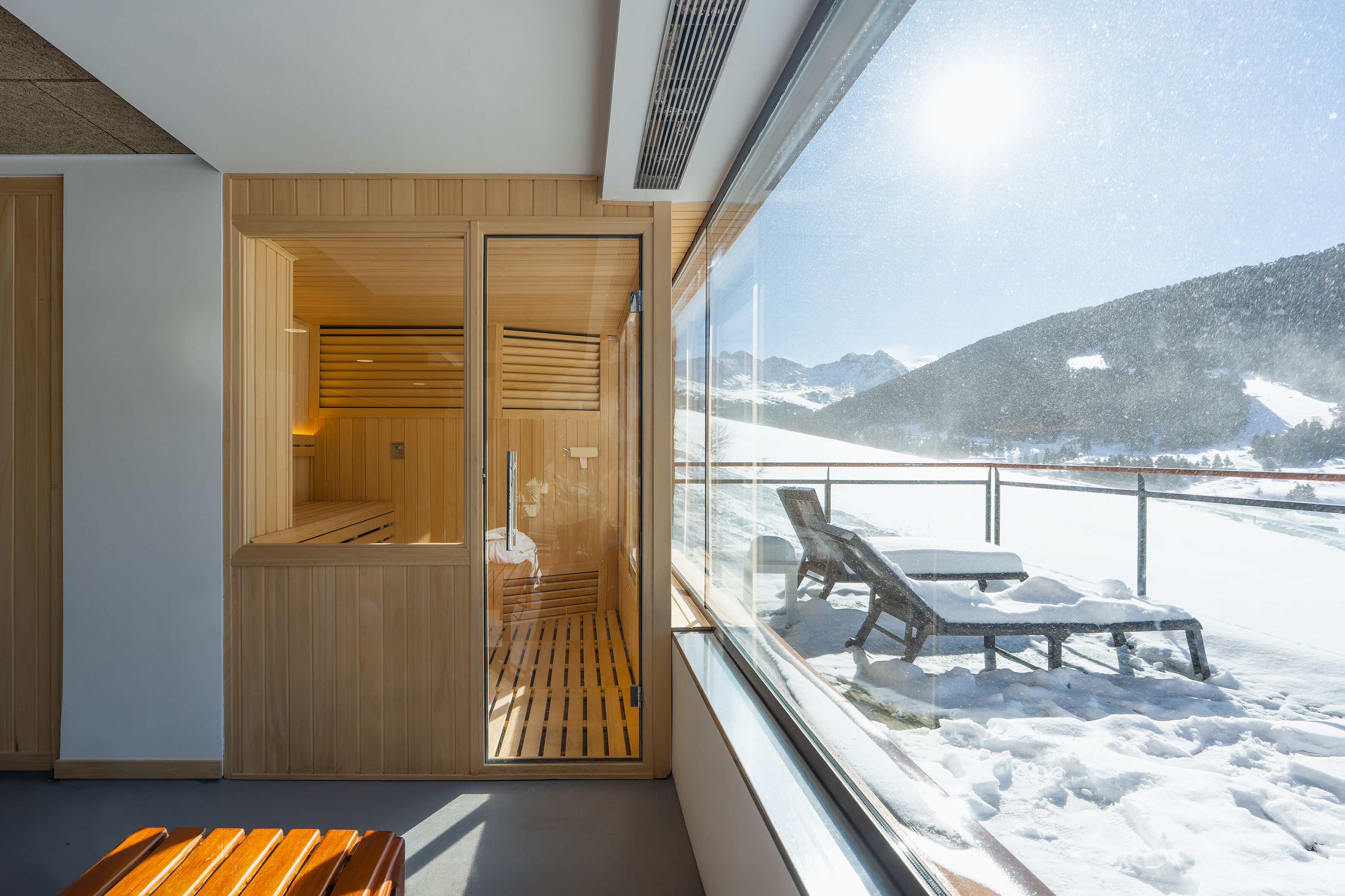 Uma sala de sauna com bancos de madeira e uma parede de vidro com vista para uma paisagem montanhosa coberta de neve.