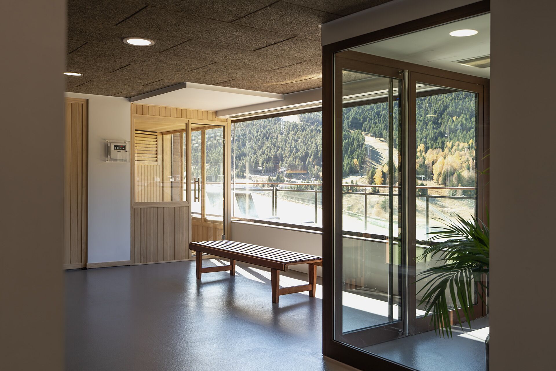A hallway with a bench, a thermostat, and large windows offering a view of a forest and a lake.