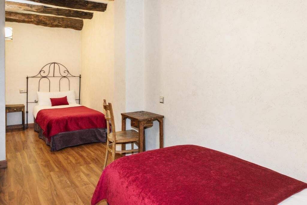 A bedroom with two beds, wooden flooring, a small wooden table, and a chair.