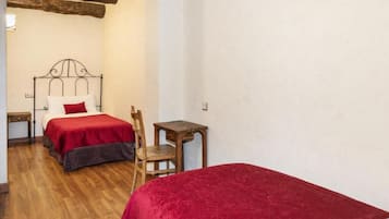 A bedroom with two beds, wooden flooring, a small wooden table, and a chair.