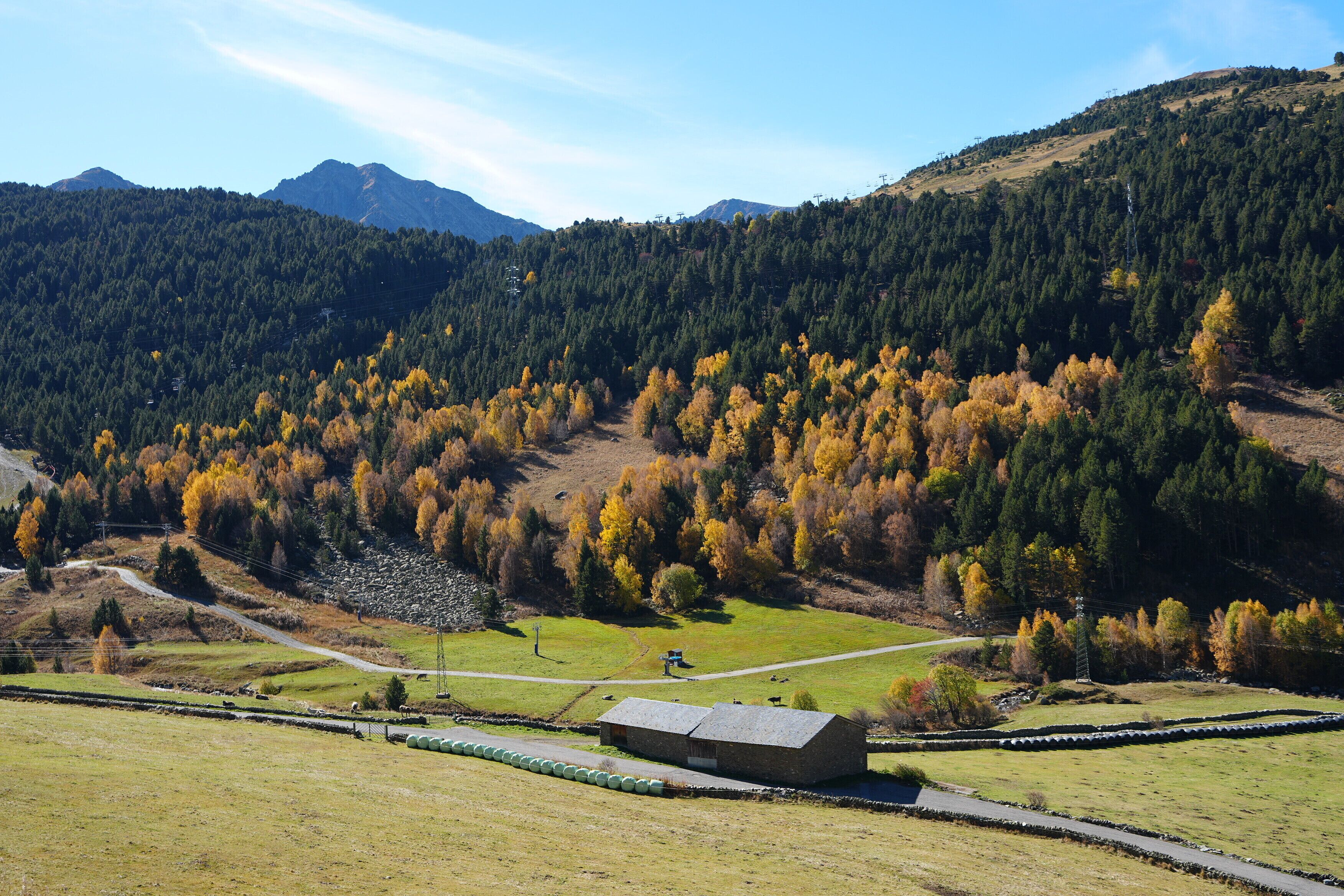 A rural landscape with a stone building, a road, and a forested hill.