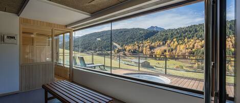 A room with a large window offering a view of a mountainous landscape with autumn foliage.