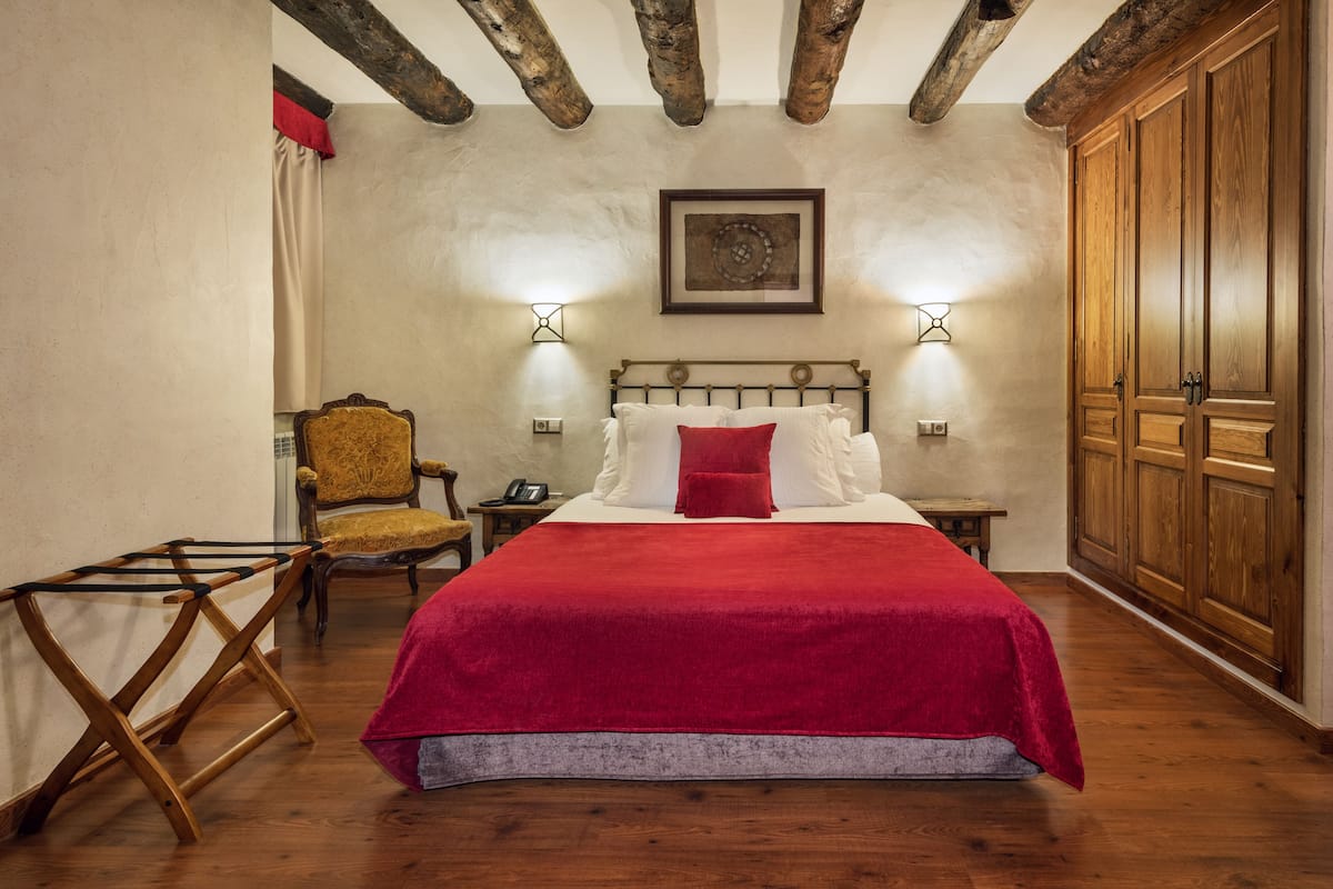 A bedroom with a wooden bed, red bedding, a wooden chair, a nightstand, and a wardrobe.