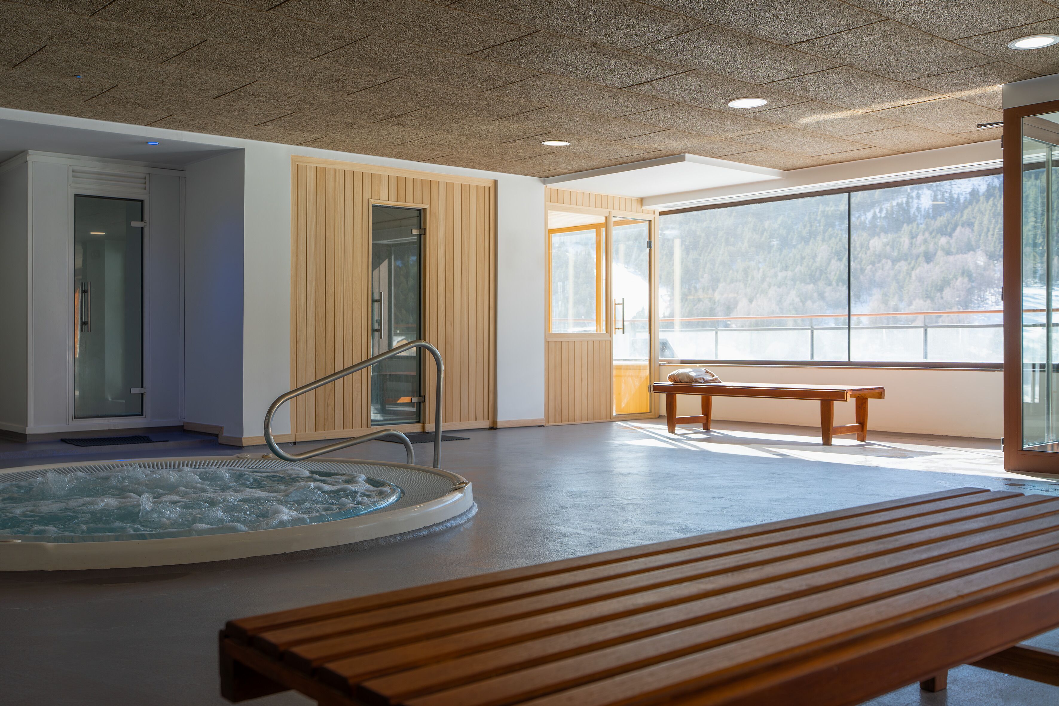 A spa area with a hot tub, wooden benches, and large windows offering a view of a mountainous landscape.