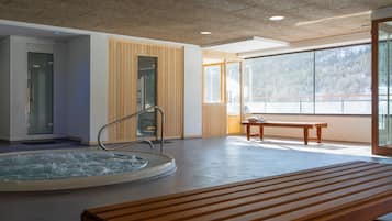 A spa area with a hot tub, wooden benches, and large windows offering a view of a mountainous landscape.