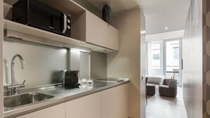 A modern kitchen with stainless steel appliances, a built-in sink, and a countertop. There is a seating area with a sofa and a chair visible through an open door. - Brera Apartments in San Babila (Milan)