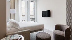 A hotel room with a bed, a TV mounted on the wall, and two armchairs. - Brera Apartments in San Babila (Milan)