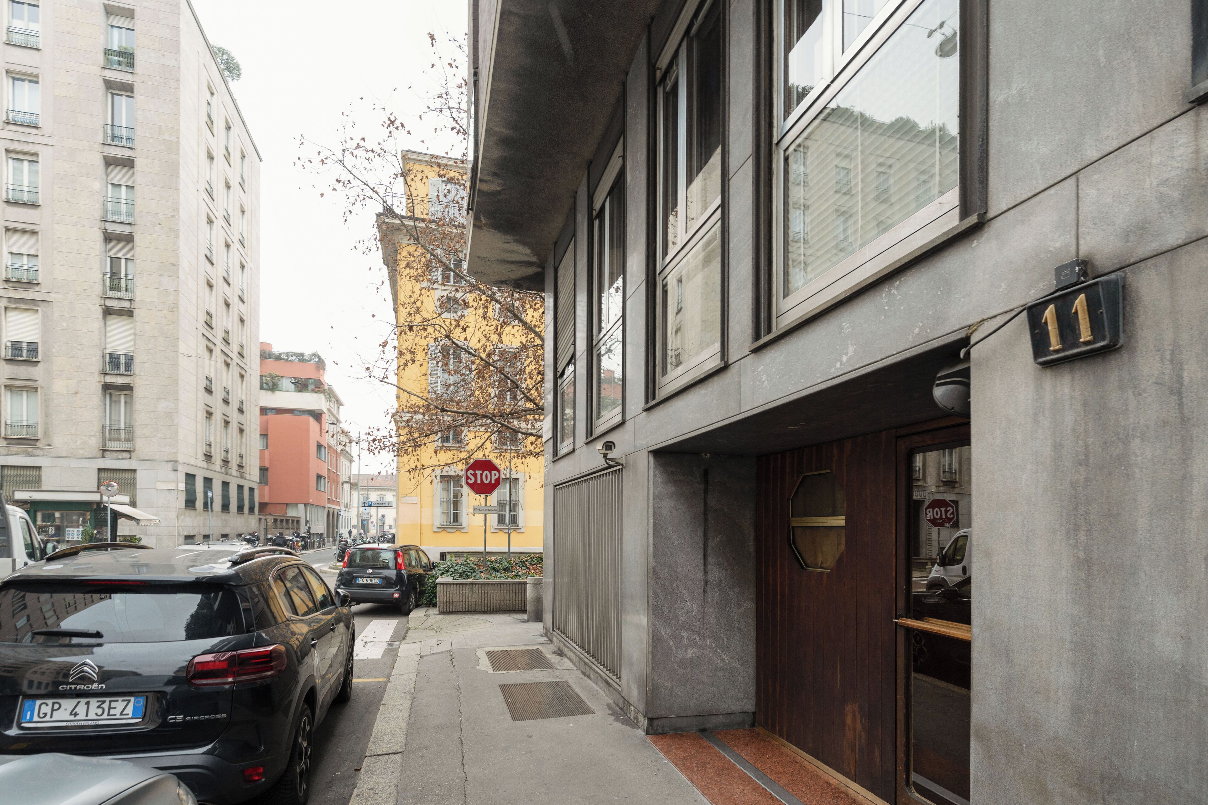 A narrow urban street with parked cars, a building with a visible door and windows, and a stop sign.