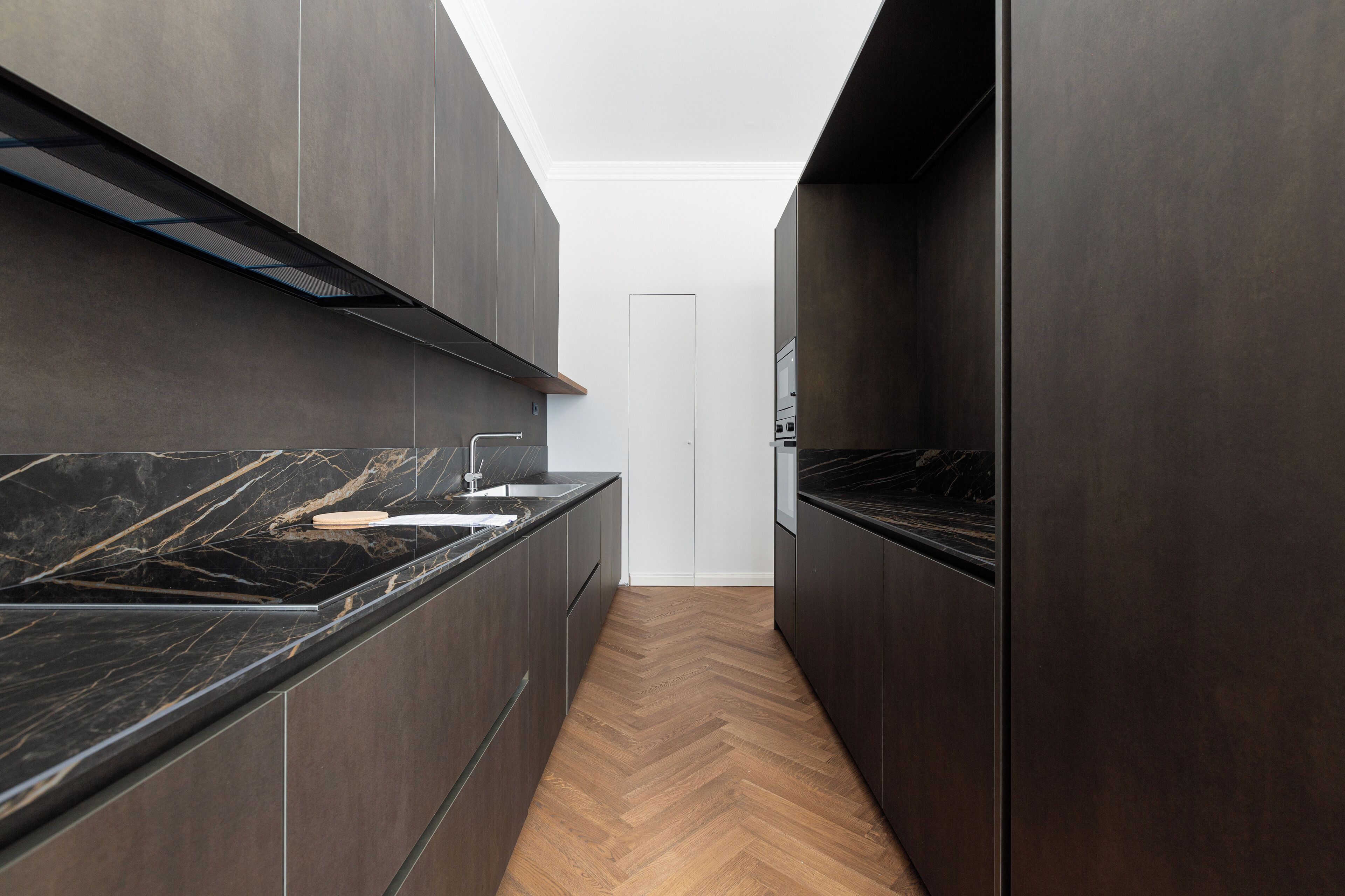 Una cocina estrecha con armarios oscuros, piso de madera en espiga y tragaluces.