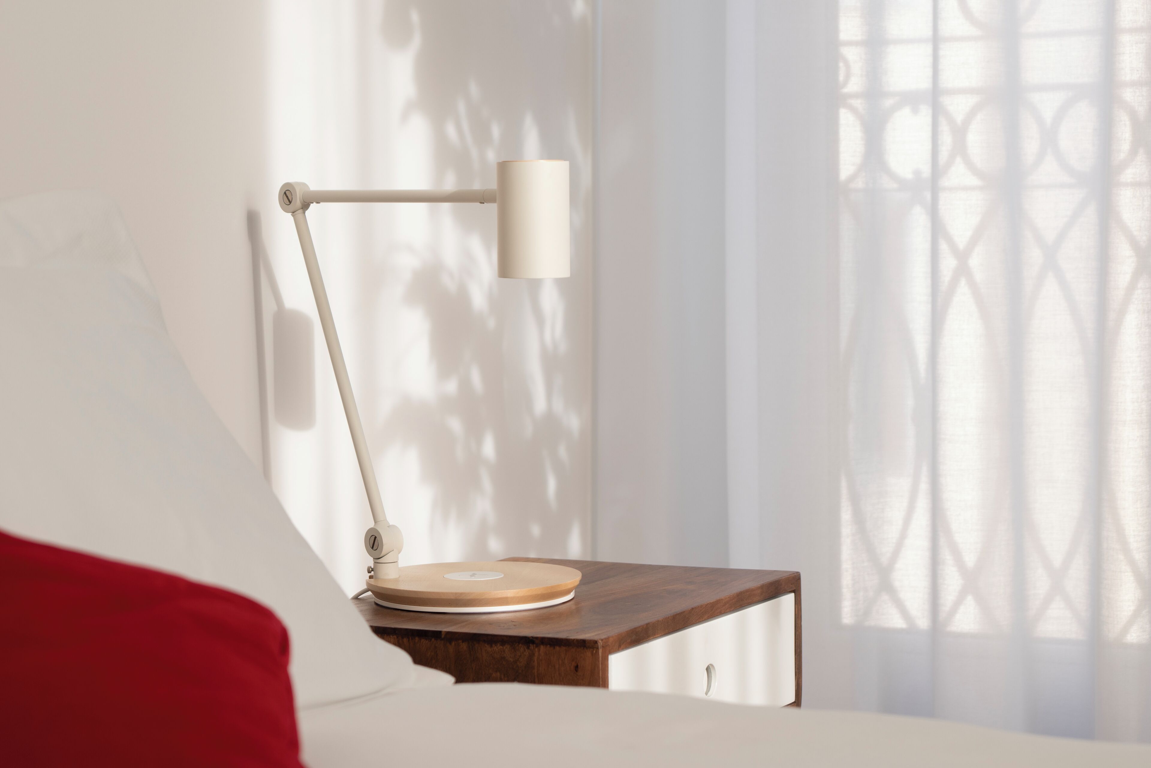 A bedside table with a lamp, a wooden nightstand, and a red pillow.