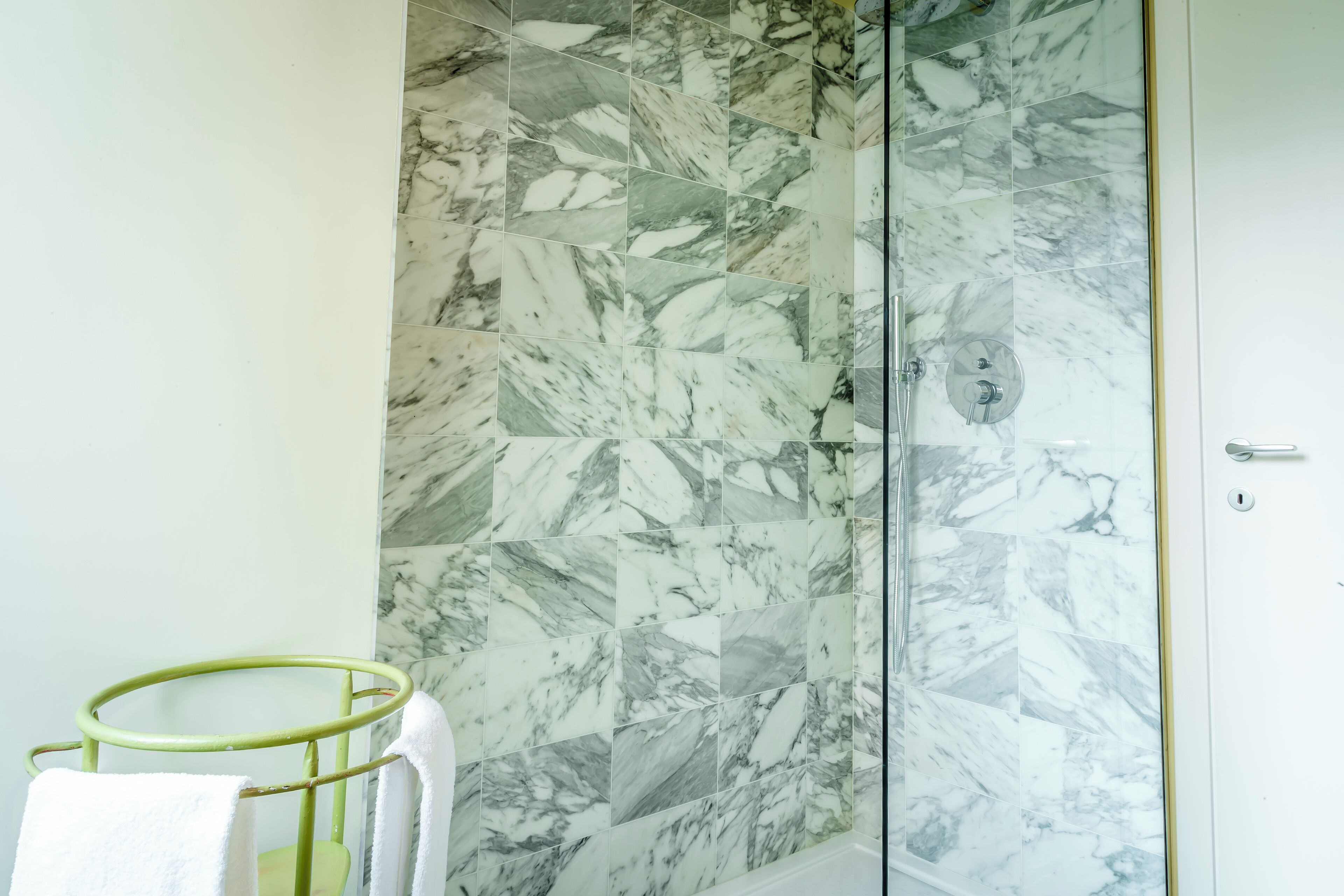 A bathroom with a shower area featuring marble tiles and a green towel rack with a white towel.