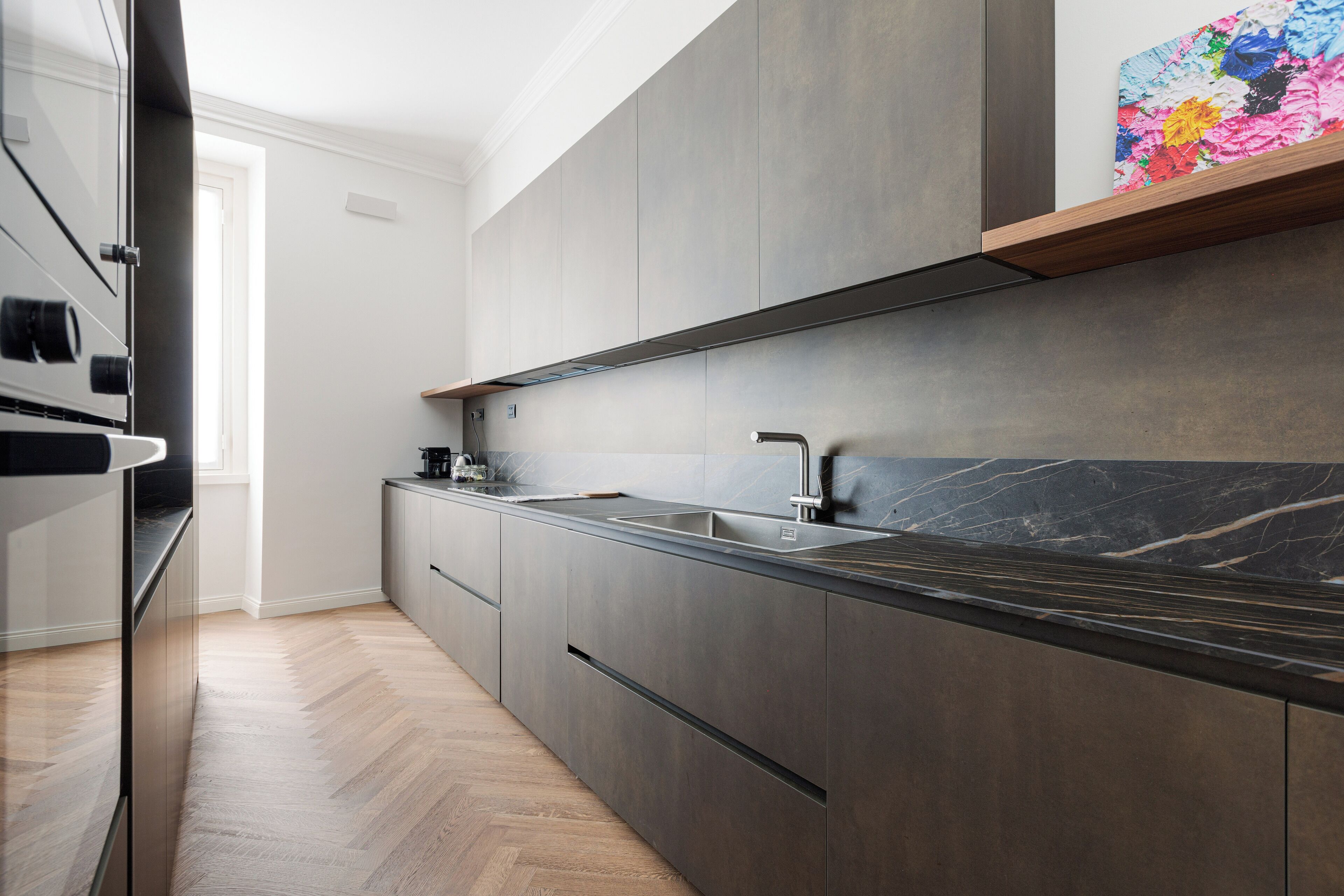 A modern kitchen with a marble countertop, stainless steel appliances, and a herringbone wood floor.