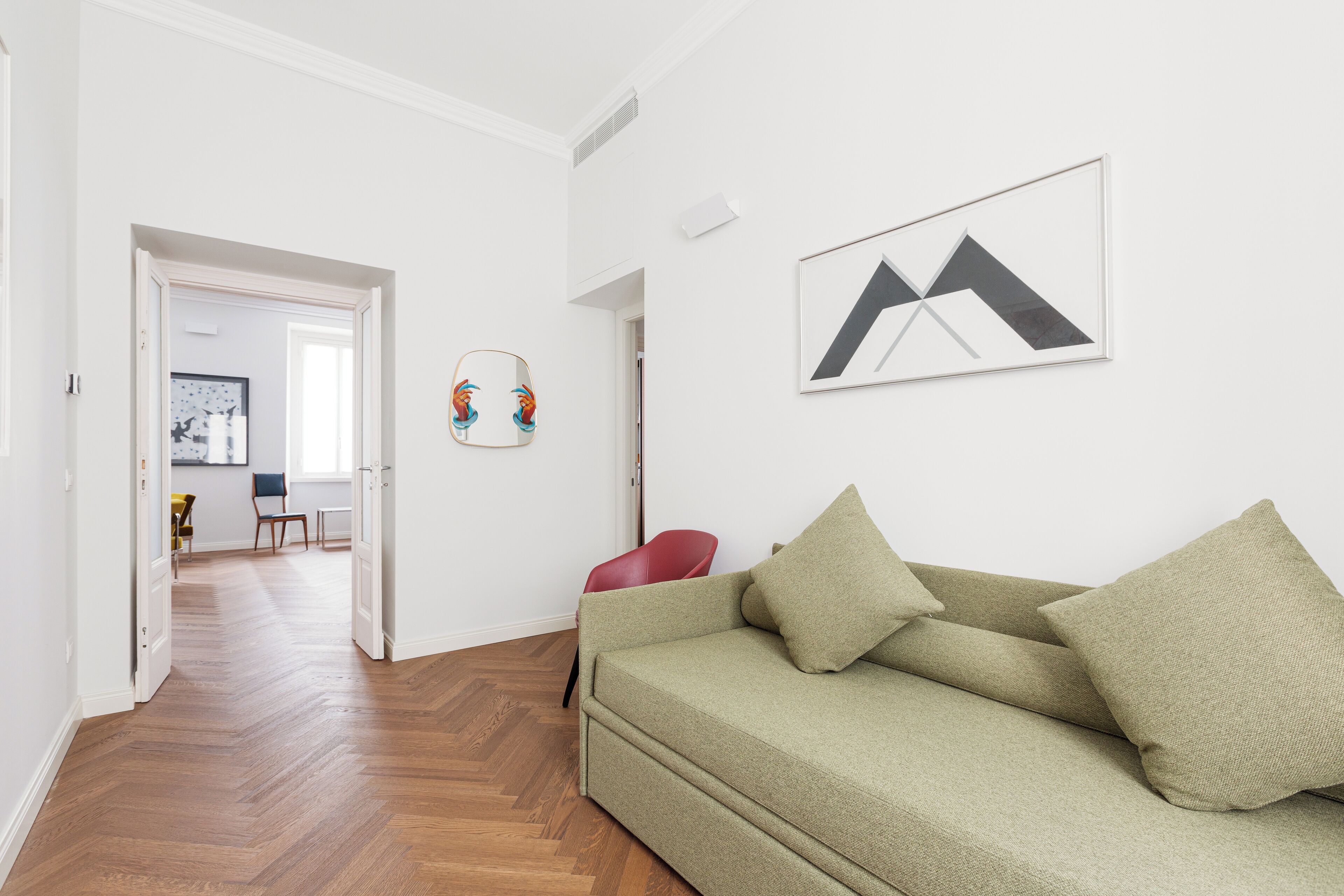 Un salon moderne avec un canapé, un fauteuil rouge et une œuvre d’art abstraite encadrée accrochée au mur.