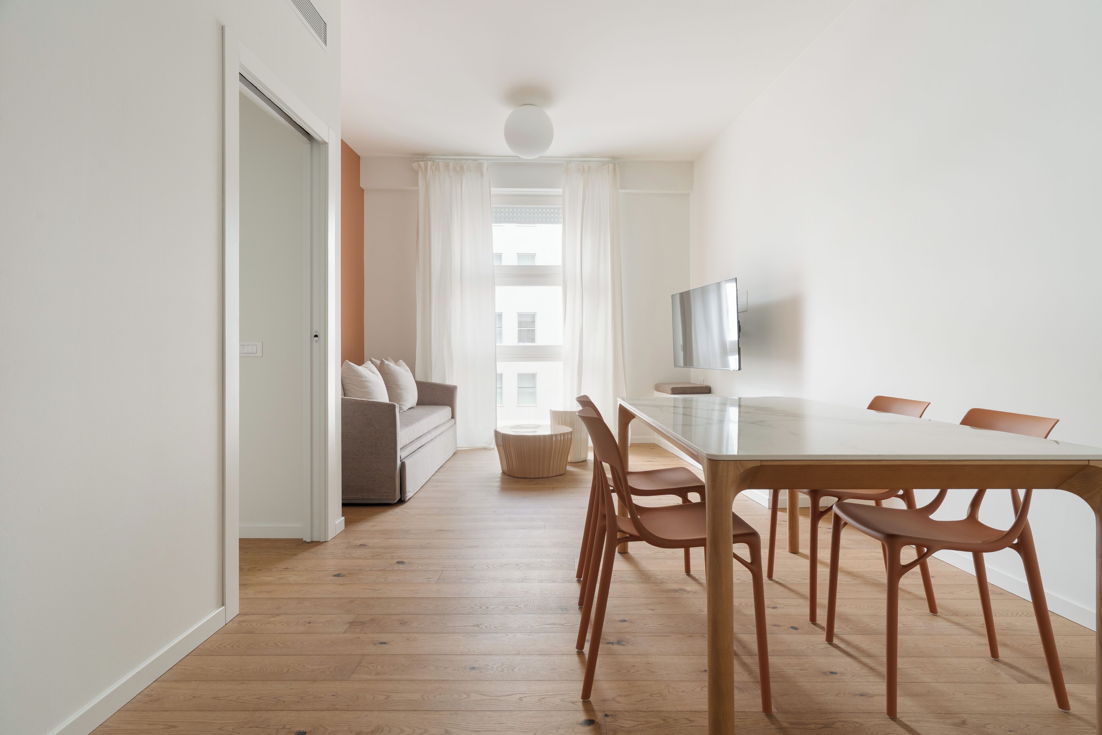 A modern living room with a sofa, a dining table with chairs, a TV, and a window with curtains.