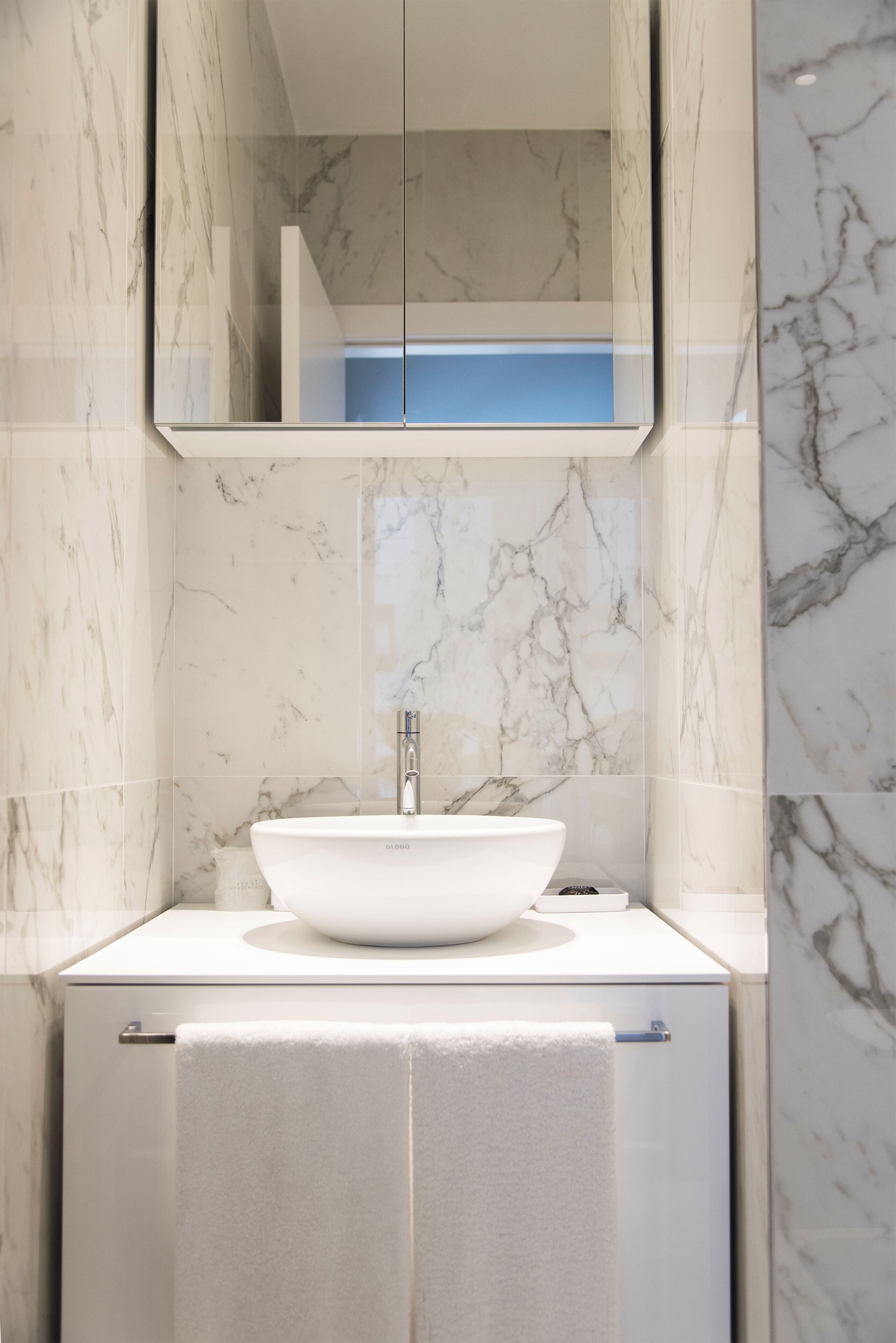 Un bany amb un lavabo blanc, un mirall a sobre i parets de marbre.