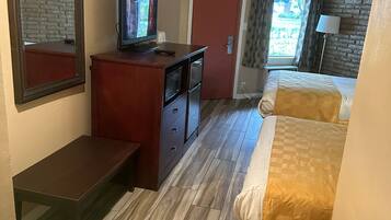 Habitación de hotel con piso de madera, un escritorio con televisor, dos camas con ropa de cama a cuadros, una puerta roja y una ventana con cortinas.