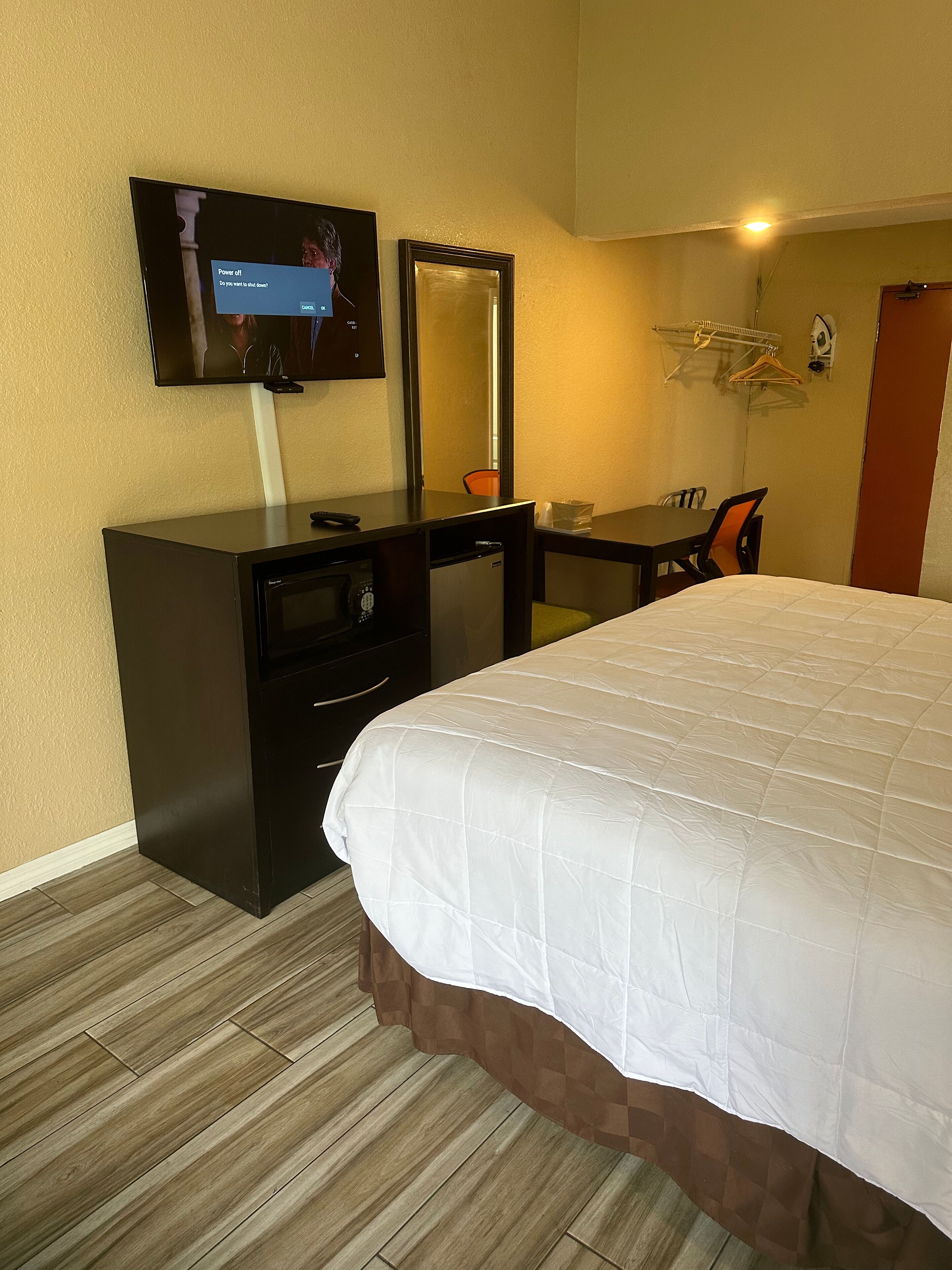 A hotel room with a bed, a desk with a chair, a television, a mirror, and a wardrobe.