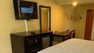 A hotel room with a bed, a desk with a chair, a television, a mirror, and a wardrobe.