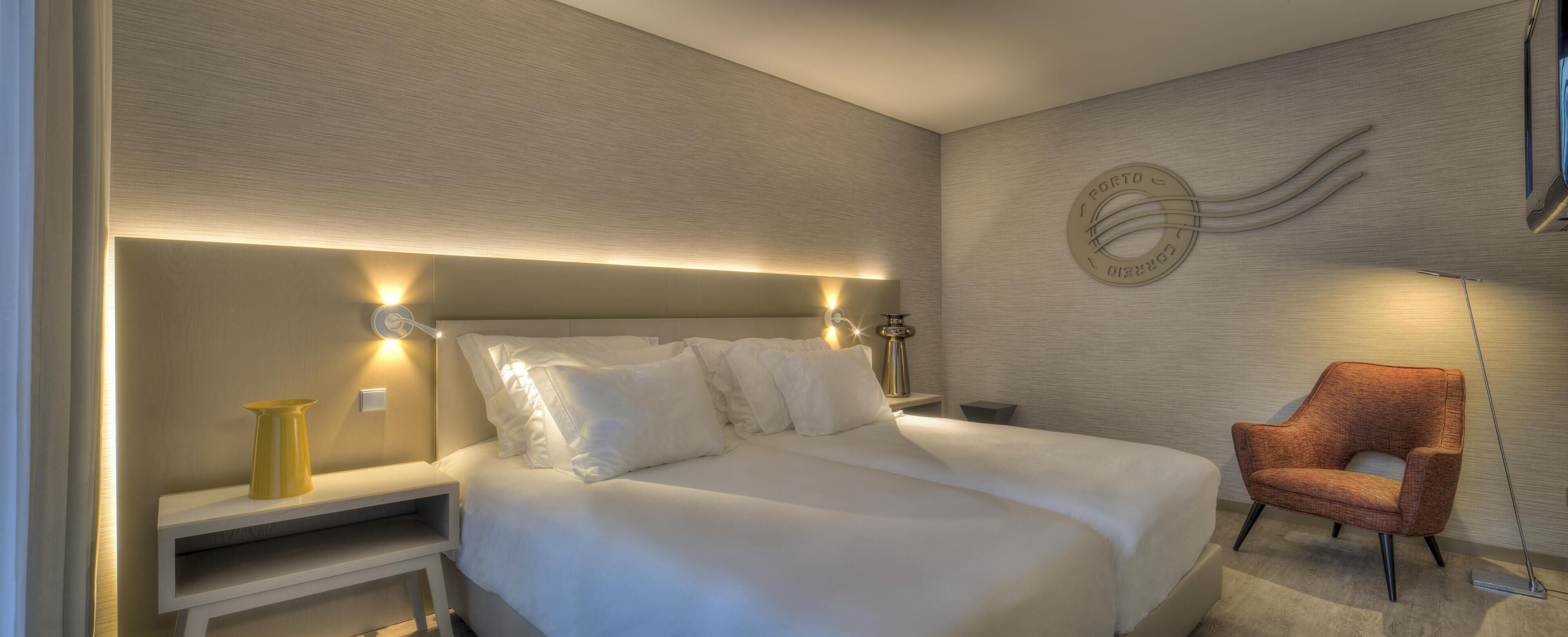 A hotel room with a bed, bedside tables, a chair, and a wall-mounted light fixture.