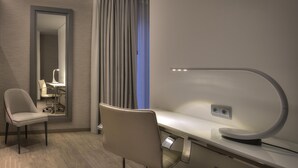 Een moderne hotelkamer met een bureau, stoel en een grote spiegel.