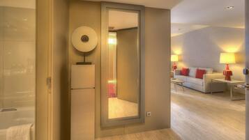 Habitación de hotel con un espejo grande, un sofá, dos mesitas de noche con lámparas y suelo de madera.