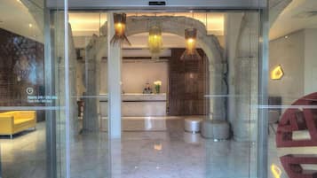 A modern hotel lobby with a reception desk, a receptionist, and a stone archway.