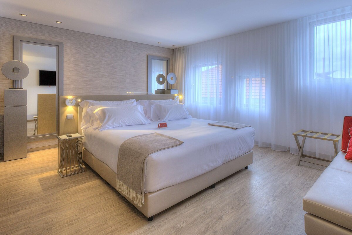 Una habitación de hotel moderna con una cama grande, una mesita de noche, un escritorio pequeño y una silla roja.